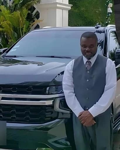 Dwane Darling of Elite Transport in a formal vest and tie beside his black Chevrolet Tahoe in Nassau